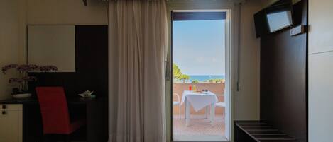 A hotel room with a bed, a desk with a chair, a TV mounted on the wall, and a balcony with a table and chairs.