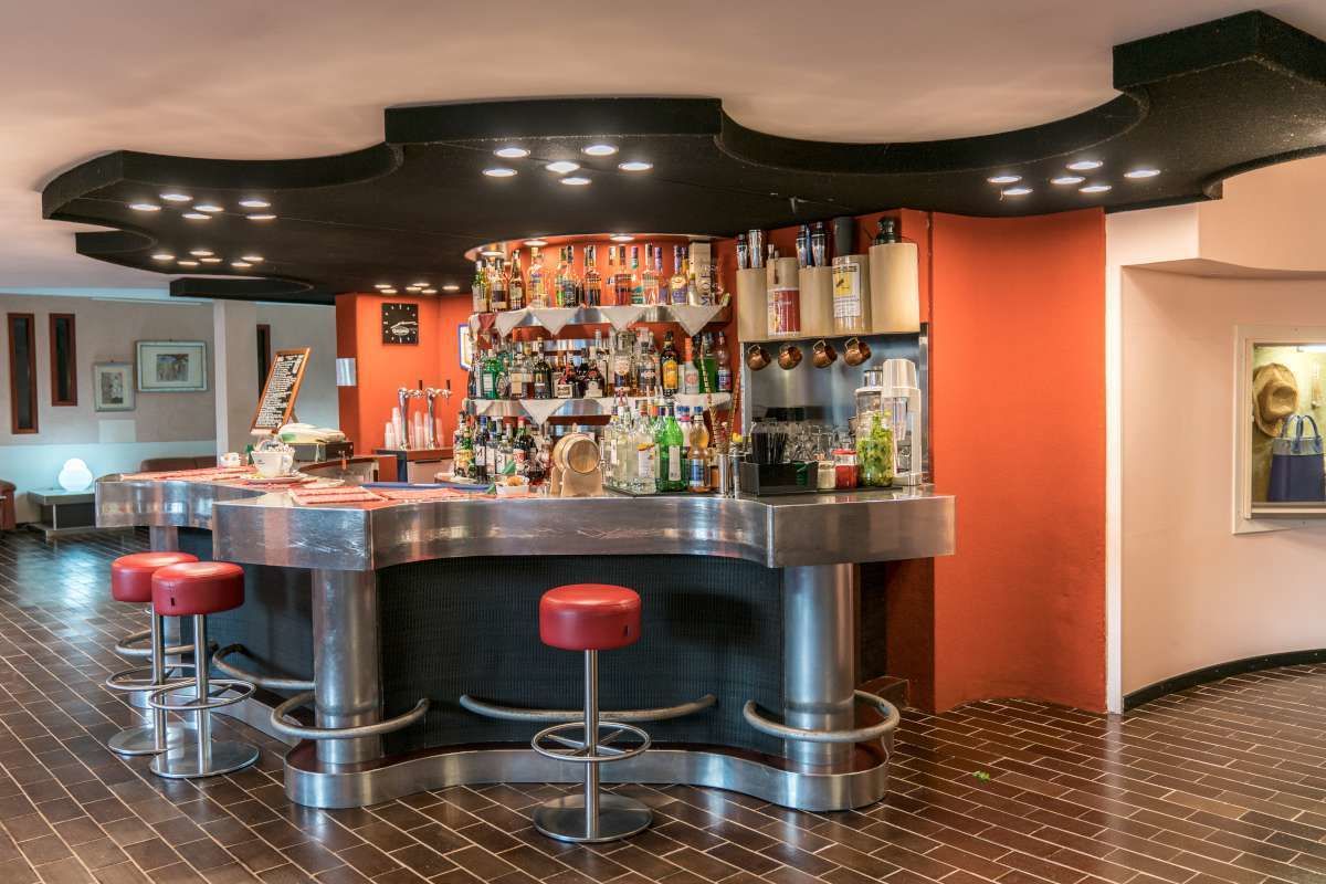 Zona de bar con mostrador curvo, varios taburetes y una amplia variedad de botellas y copas.