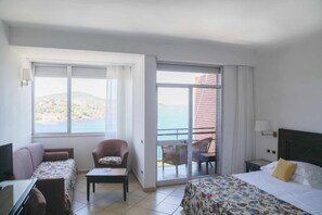 A hotel room with a bed, a sofa, a chair, a small table, and a balcony with a view of the sea. - JR Resort Elba International (Capoliveri)