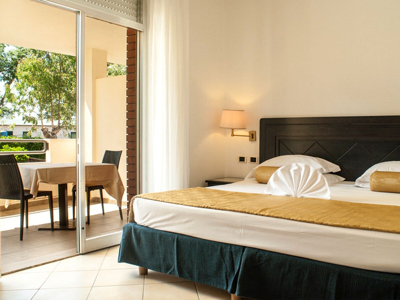 Ein Hotelzimmer mit einem Bett, einem Tisch mit Stühlen, einer Lampe und Blick auf Grünfläche.