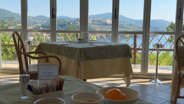 Ein Esstisch mit Frühstücksangeboten, Blick auf Berge und Wasser, und ein Schild, das ein Restaurant anzeigt.
