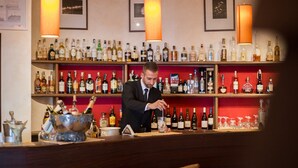 A bar with shelves stocked with various bottles, a bartender preparing a drink, and a bar counter with glasses and a decorative bowl. - JR Resort Elba International (Capoliveri)