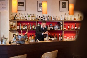 A bar with shelves stocked with various bottles, a bartender preparing a drink, and a bar counter with glasses and a decorative bowl. - JR Resort Elba International (Capoliveri)