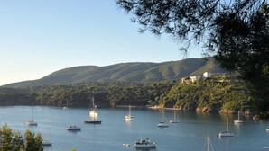 A coastal marina with multiple sailboats anchored in calm waters, surrounded by lush green hills and a clear sky. - JR Resort Elba International (Capoliveri)