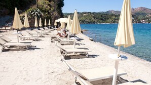 A beach with sun loungers and umbrellas, a clear blue sea, and a rocky hillside in the background. - JR Resort Elba International (Capoliveri)