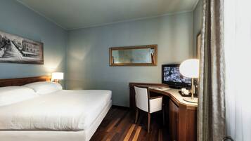 A hotel room with a bed, desk, chair, television, and a painting on the wall.