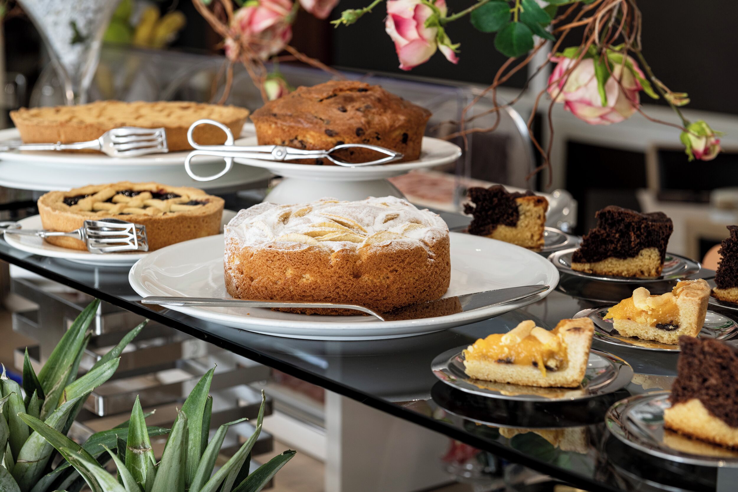 Una mesa de buffet con diversos postres, incluyendo pasteles y tartas, dispuestos en platos y fuentes.