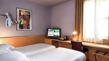A hotel room with two beds, a desk with a computer, a television, and a window with curtains.