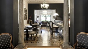 A hallway with a patterned floor, a chandelier, and a dining area with chairs and tables. - Albergo Celide (Lucca)