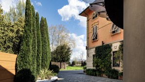 A building with a garden pathway leading to a door, surrounded by tall trees and a clear sky. - Albergo Celide (Lucca)
