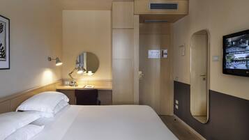 A hotel room with a bed, a desk with a lamp, a mirror, and a television on the wall.