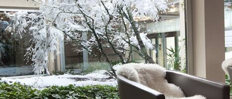 Una habitación con vistas a un árbol cubierto de nieve a través de una ventana, un sillón con un cojín blanco mullido y un sofá de color oscuro.