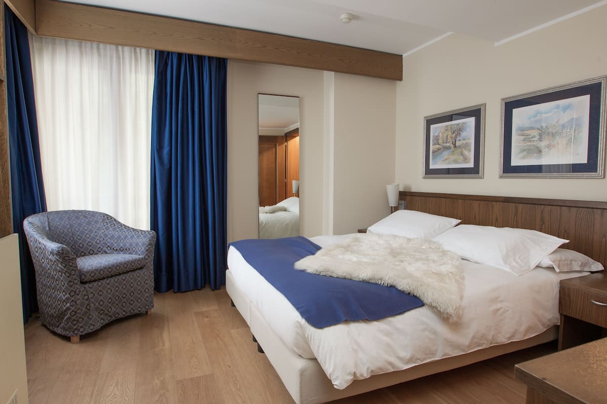 Ein Hotelzimmer mit einem Bett, einem Sessel, einem Spiegel und zwei gerahmten Bildern an der Wand.