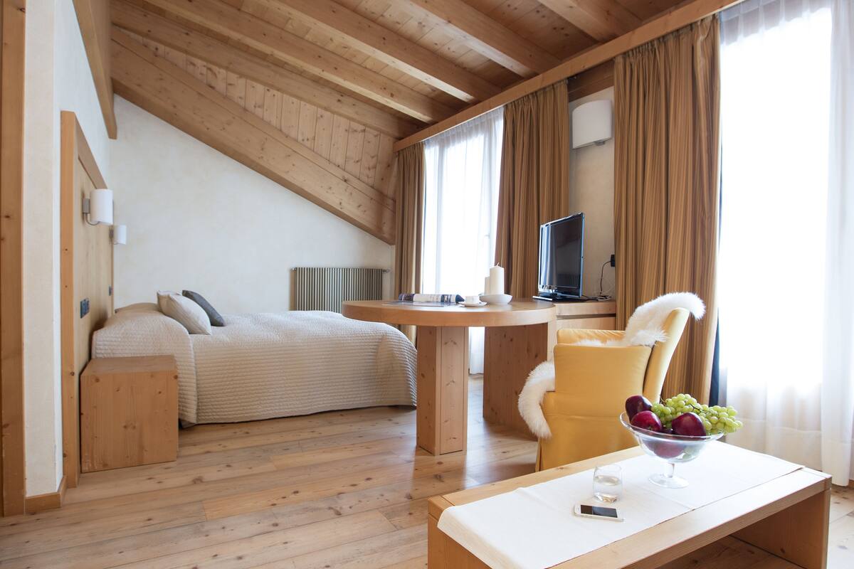 Ein gemütliches Zimmer mit einem Bett, einem Esstisch, einem Fernseher und einer Obstschale.