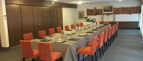 Un salón de conferencias con una larga mesa, sillas anaranjadas y un mantel de color neutro.