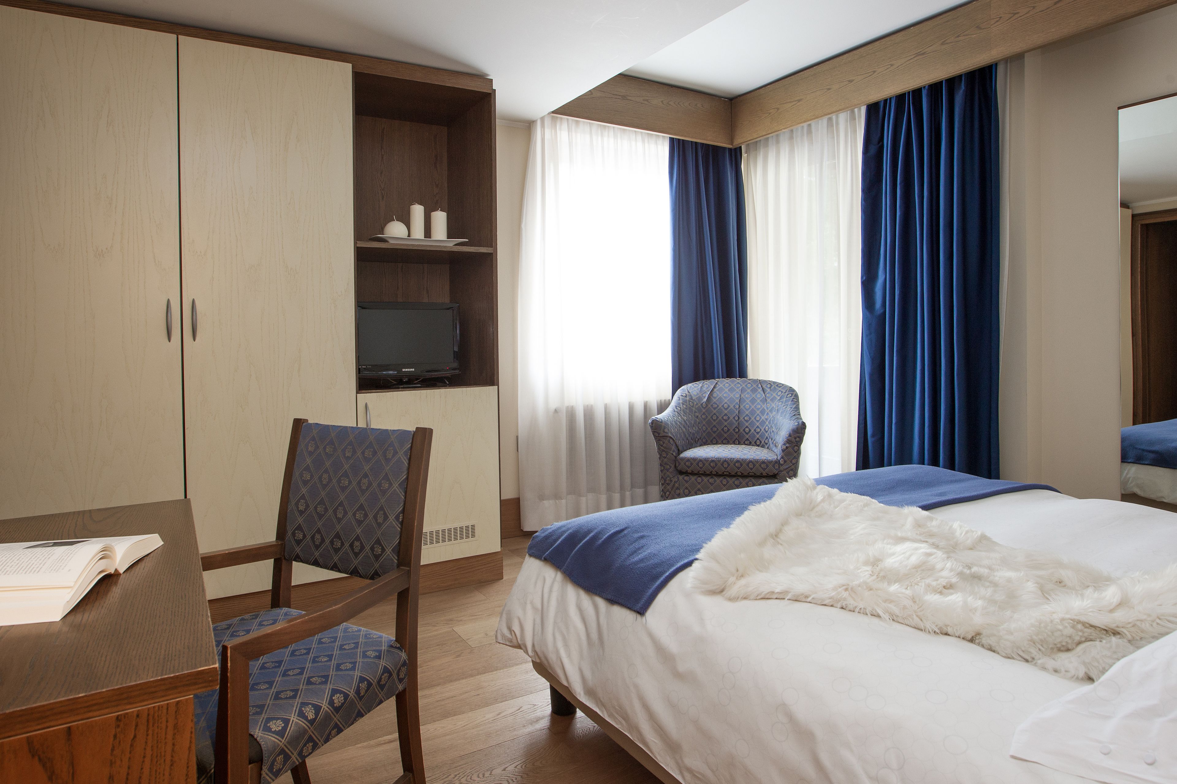 Een hotelkamer met een bed, een bureau met stoel, een televisie en een kledingkast.