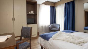 A hotel room with a bed, a desk with a chair, a television, and a wardrobe.
