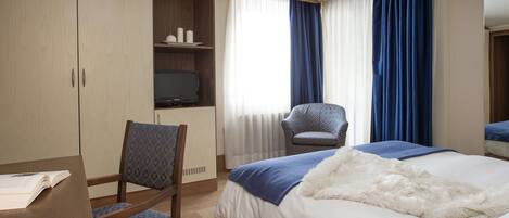 Een hotelkamer met een bed, een bureau met stoel, een televisie en een kledingkast.