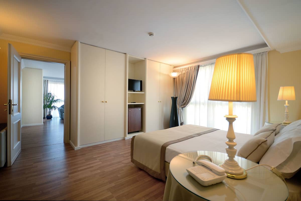 Quarto de hotel com cama, mesa de cabeceira com abajur, telefone, televisão sobre uma estante e guarda-roupa.