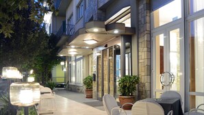 An outdoor seating area with tables and chairs, potted plants, and a stone facade. - Ambasciatori Palace (Montecatini Terme)