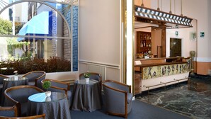 A lobby with round tables and chairs, a reception desk, and a large window overlooking the street. - Ambasciatori Palace (Montecatini Terme)