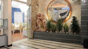 A lobby with a stone wall, a large mirror, a statue, and a dining area visible through an open door. - Ambasciatori Palace (Montecatini Terme)