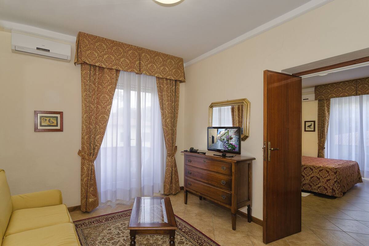 A hotel room with a sofa, a wooden dresser, a television, and a bed.