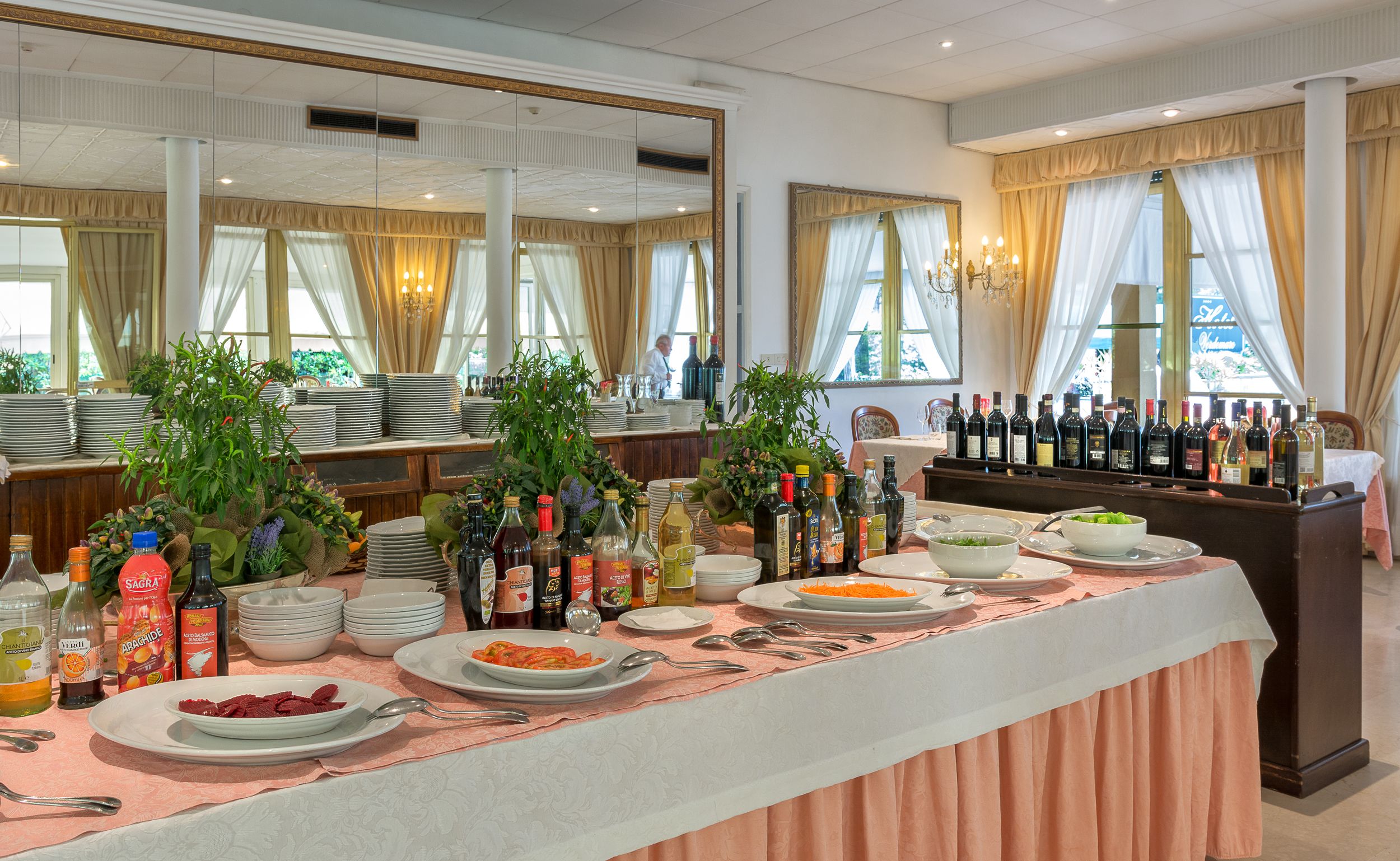 Disposição de buffet com diversos pratos, garrafas de bebidas e um espelho refletindo o ambiente.