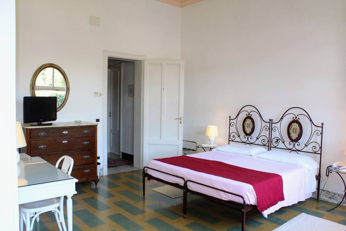A bedroom with a bed, a dresser, a television, and a desk.
