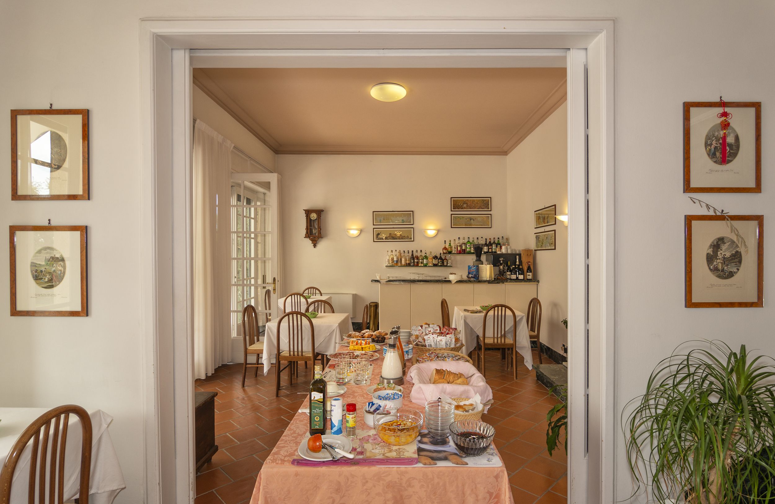 A dining area with a table set for a meal, chairs, a clock, and framed pictures on the walls.