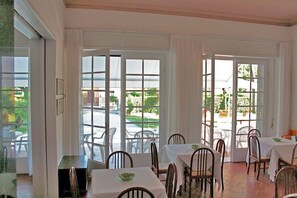A dining area with tables and chairs, large windows with curtains, and a view of the outside. - Hotel Villa Edera (Camaiore)