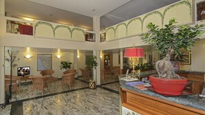 A hotel lobby with a marble floor, wicker furniture, a reception desk, and a large potted plant. - Hotel Katy (Viareggio)