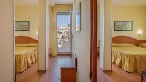 A hotel room with two beds, a view of the city through a balcony door, and a wooden staircase. - Hotel Katy (Viareggio)