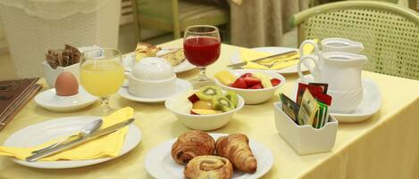 A breakfast table with plates of croissants, fruit, and a jug of juice.