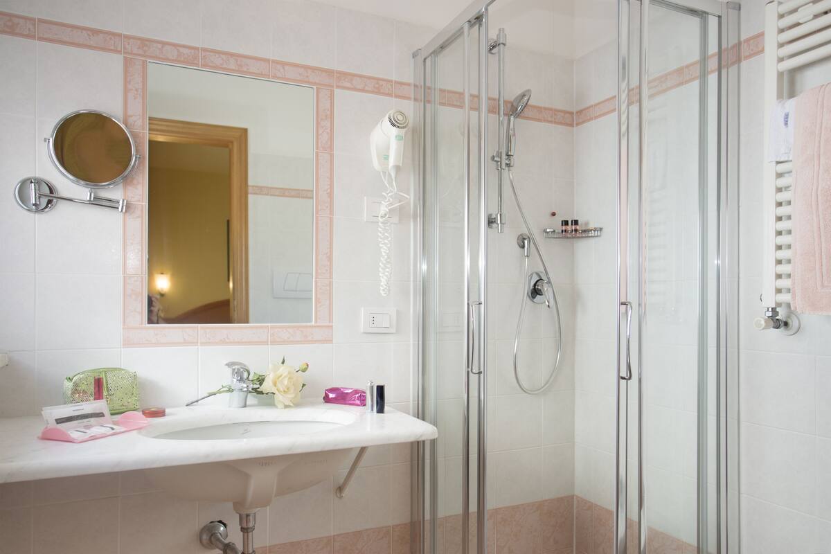 A bathroom with a glass shower enclosure, a sink with a mirror, and toiletries on the counter.