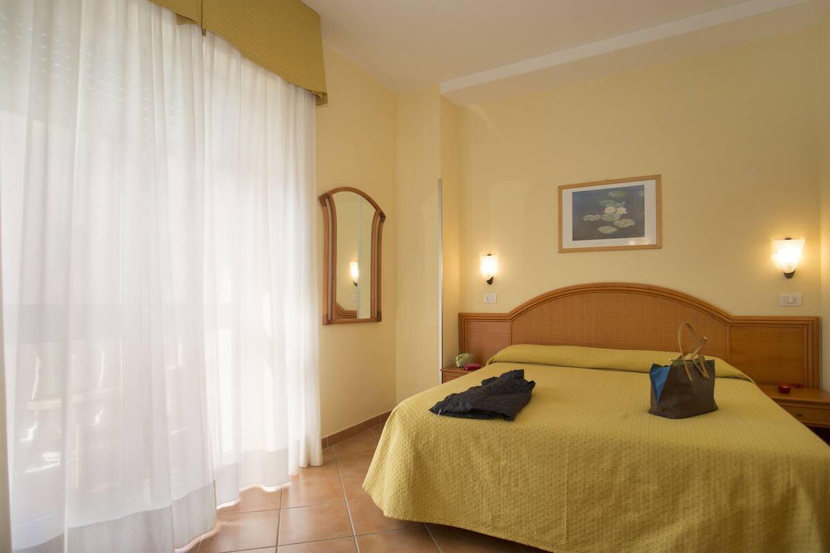 A hotel room with a bed, a nightstand, a lamp, a mirror, and a painting on the wall.