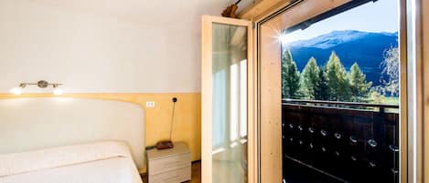 A bedroom with a bed, bedside table, and a large window with a view of mountains.