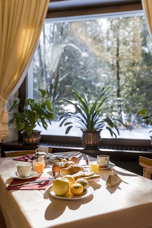 A breakfast table with a variety of food items, a window with a view of trees, and a potted plant on the windowsill.