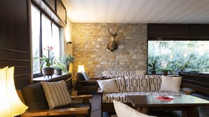 A cozy lounge area with wooden furniture, a stone wall, and a mounted deer head.