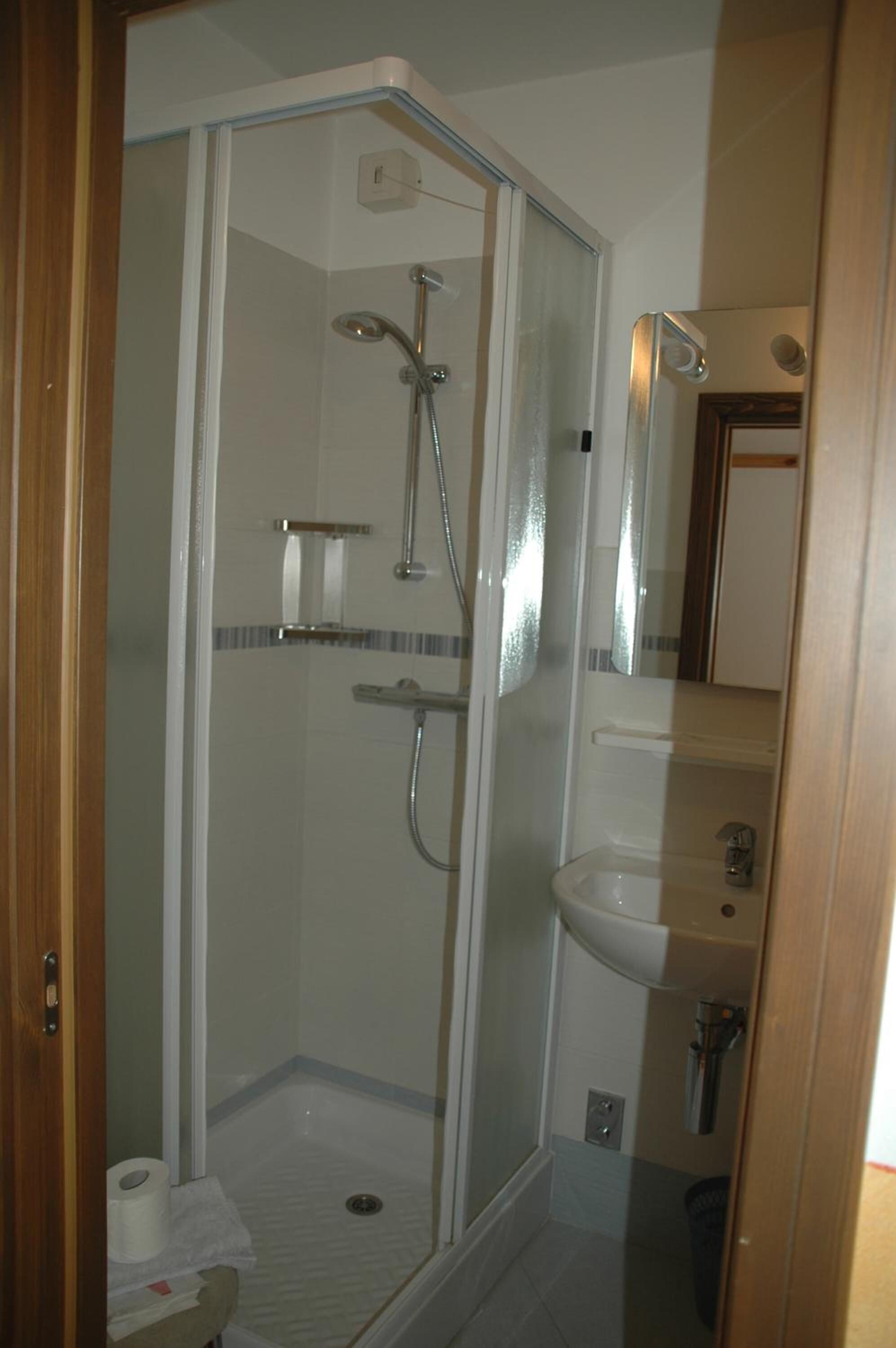 A glass-enclosed shower stall with a handheld showerhead and a wall-mounted faucet.