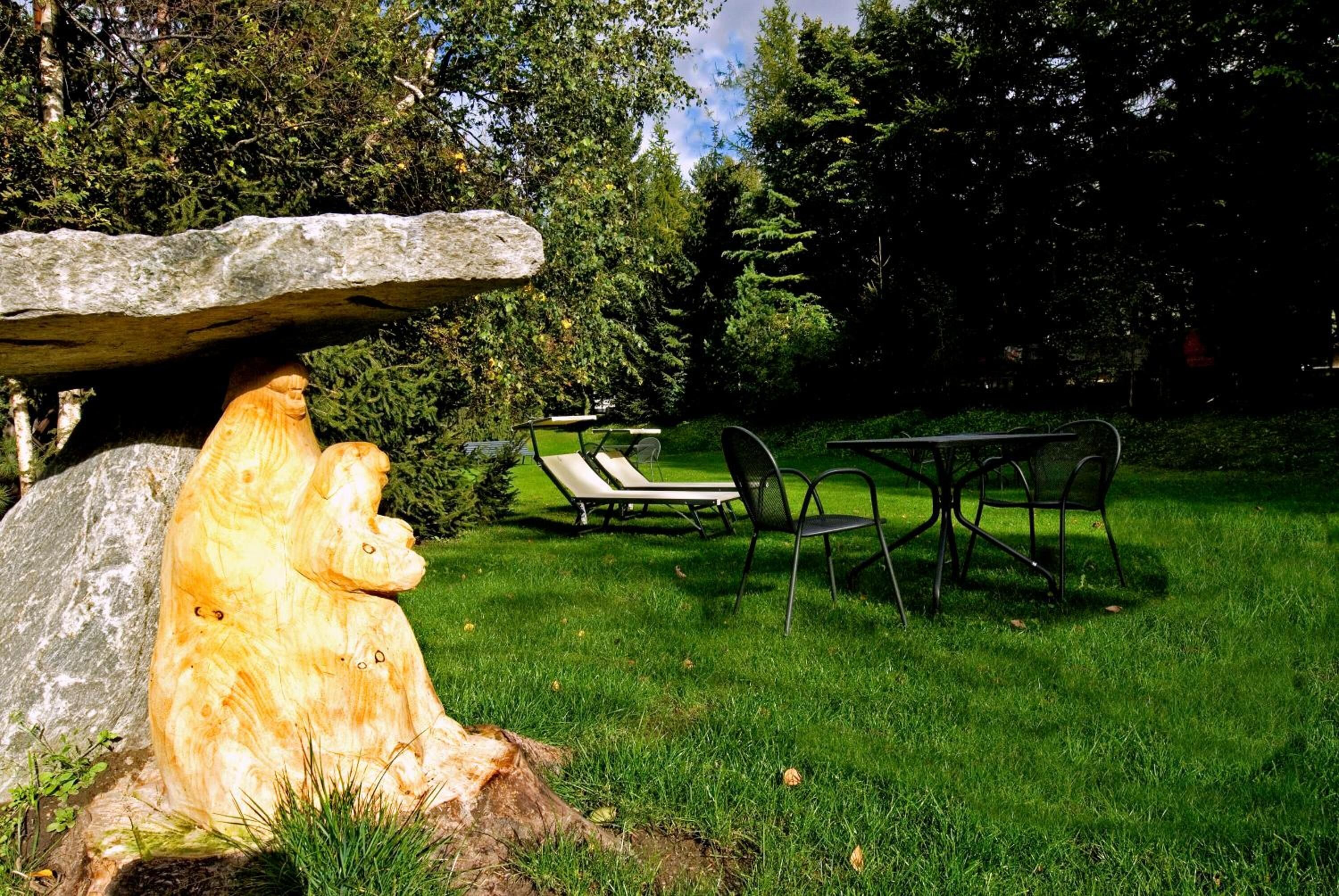 A garden with a large rock sculpture, a table with chairs, and a grassy area.