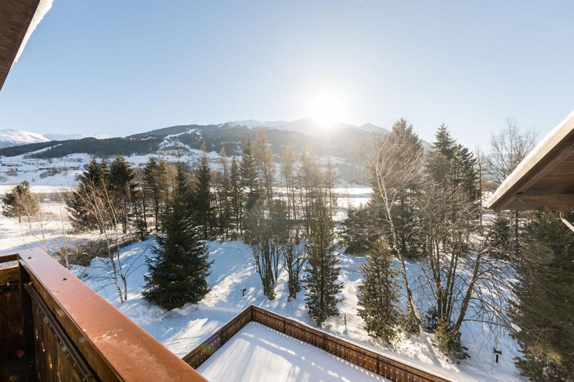 A snowy landscape with a mountain in the background and a wooden deck in the foreground.