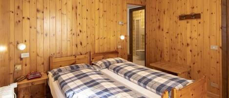 Un dormitorio con paneles de madera, dos camas, una mesita de noche y una pequeña mesa.