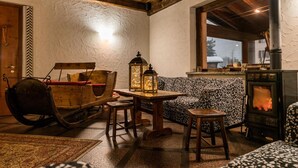 A cozy room with a rustic wooden ceiling, a patterned sofa, a rocking chair, a small table with lanterns, and a fireplace.