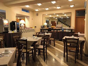 A hotel dining area with multiple tables and chairs, a coffee machine, and a counter with food items. - Ai Tufi (Siena)