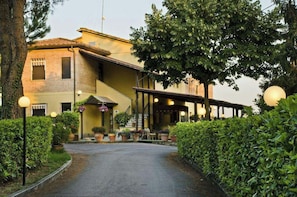 A building with a covered entrance, potted plants, and a pathway leading to the entrance. - Ai Tufi (Siena)