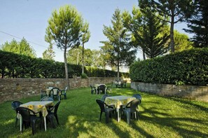 An outdoor seating area with tables and chairs, surrounded by trees and a stone wall. - Ai Tufi (Siena)
