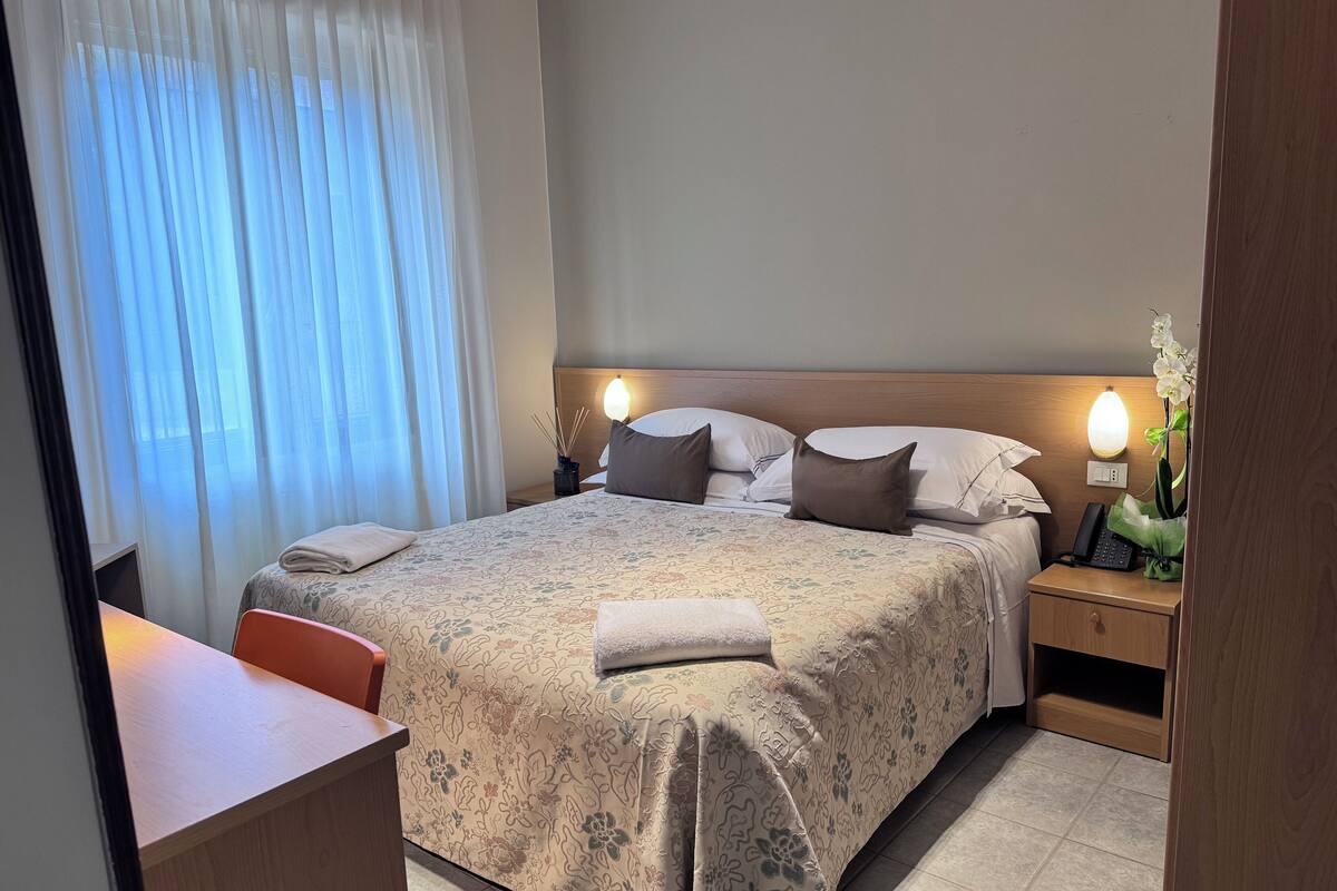 A neatly made bed with floral bedding, a bedside table with a lamp, and a chair.