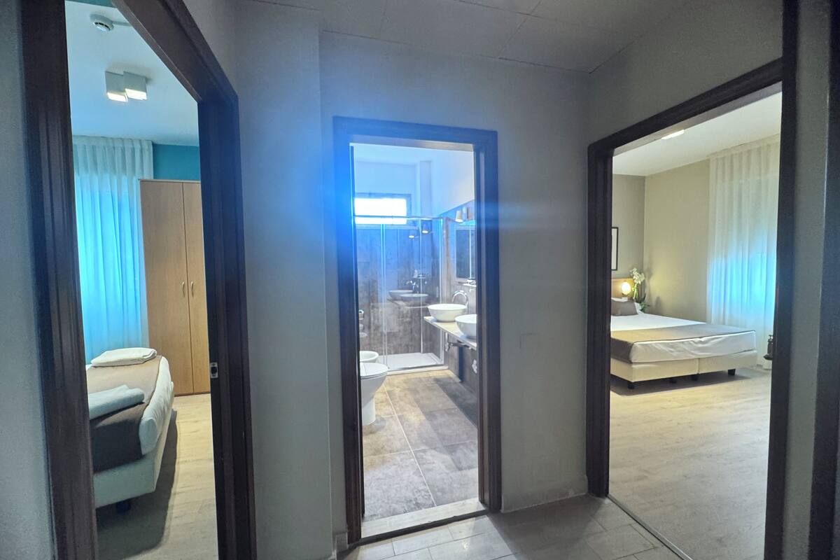 A hotel room with a bed, a bathroom with a sink and toilet, and a small sitting area with a chair.