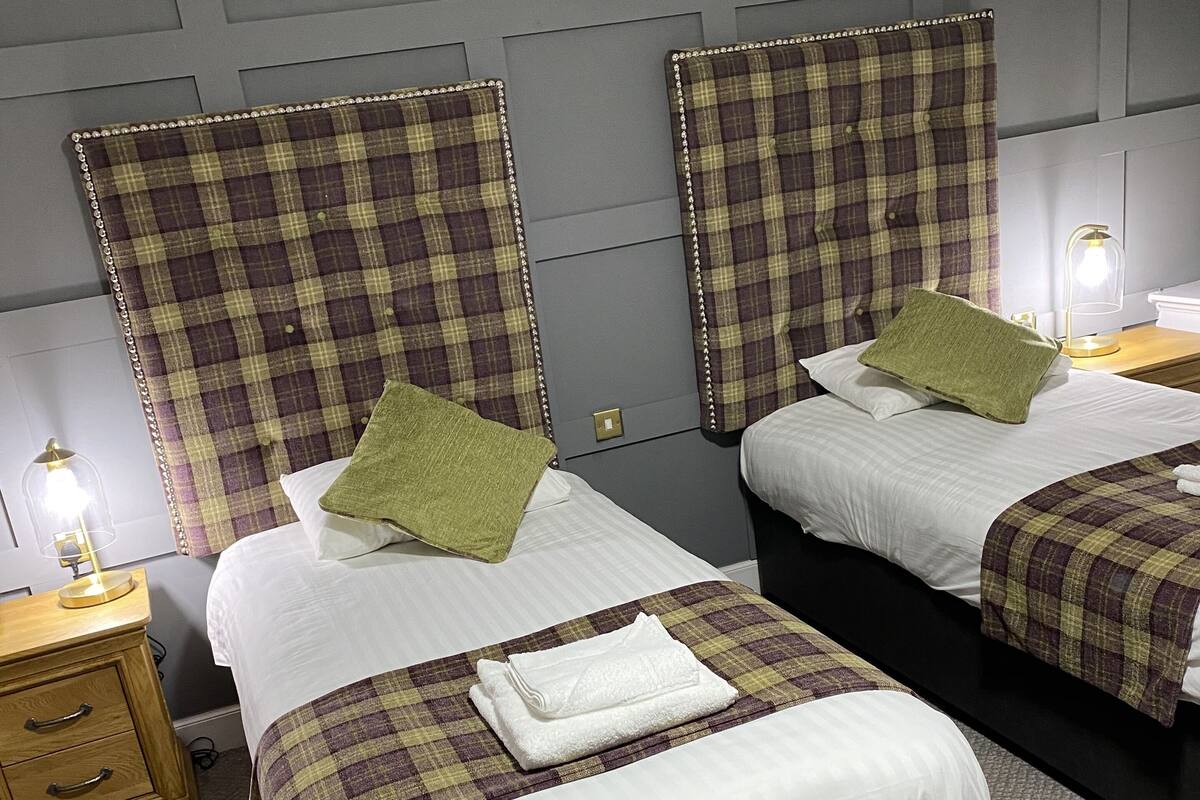 A hotel room with two beds, each with a plaid headboard, a wooden nightstand, and a lamp.
